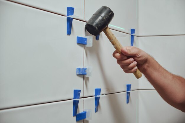 Tiler knocks the wedges of the ceramic tile leveling system off the wall in the bathroom