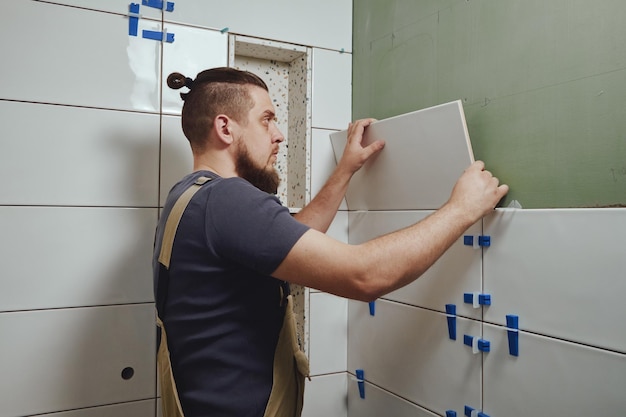 Photo tiler laying installing ceramic tiles on the wall in the bathroom