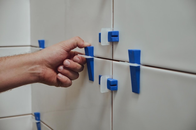 Tiler using tile leveling system when laying ceramic tiles on bathroom wall