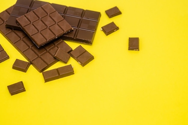 Плитка и кусочки молочного шоколада лежат на желтом