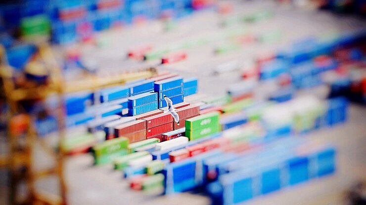 Photo tilt shift image of bird flying over cargo containers at harbor