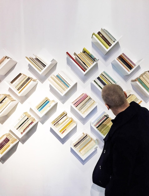 Foto tilt shot di un uomo che guarda le librerie sulla parete bianca