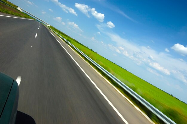 Tilted angled shot of a smooth highway surrounded by beautiful summer nature with green grass and blue sky with trees on a sunny summer hot day