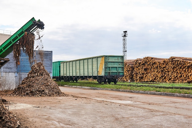 Timber yard with stacks of logs, open freight wagons and bark\
chipper