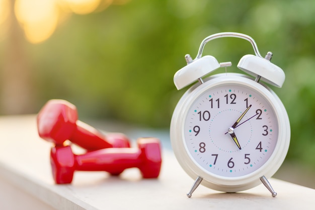 Time 5 morning for exercising alarm clock and dumbbells on green natural background outside