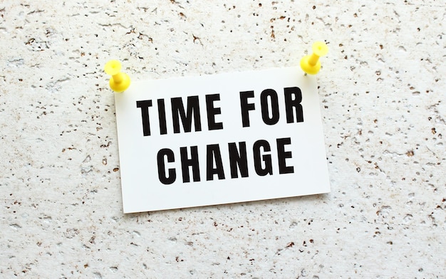 Time for change is written on a card attached to a white textured wall with a button office reminder