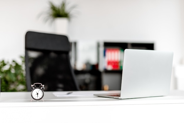 Time concept in the company office workplace, alarm clock and laptop on the desk