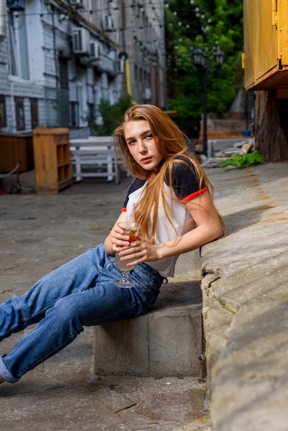 È ora di bere un cocktail. una donna molto bella beve un cocktail. bionda naturale in maglietta e jeans