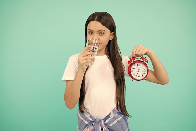 体の水分補給の活力で水を飲む時間1日あたりの飲酒は水分補給されます子供はガラスを保持し、時計の子供は喉が渇いた十代の少女の目覚まし時計健康な子供の生活を感じます