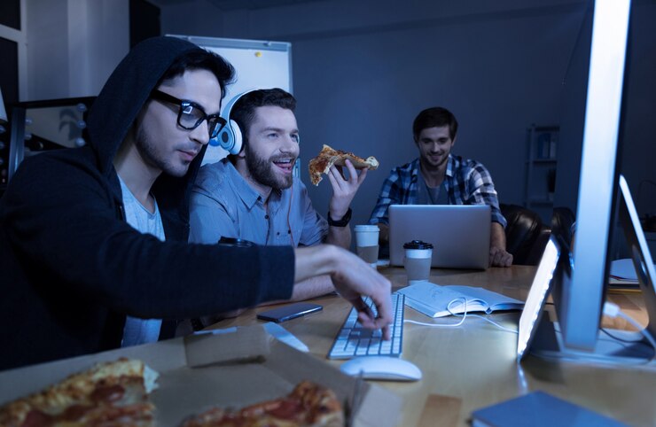 Photo time to eat. cheerful delighted positive man holding a slice of pizza and eating it while looking at the computer screen