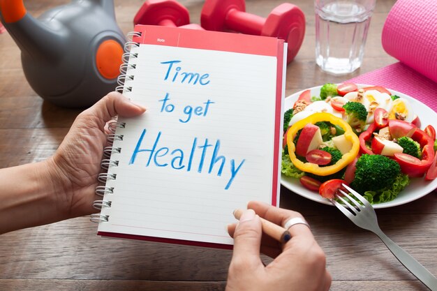 Photo time to get healthy, text on diary book with salad and fitness items on table