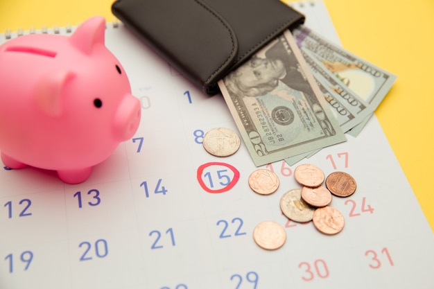 Time to invest,business concept. Pink piggy bank and wallet with money banknotes, calendar on yellow background.