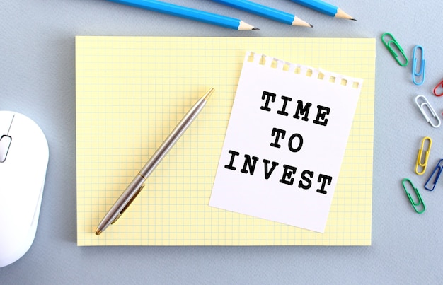 Time to invest è scritto su un pezzo di carta che giace su un taccuino accanto alle forniture per ufficio. concetto di affari.