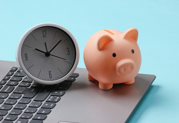 Time to invest, online business. Piggy bank with clock on laptop keyboard