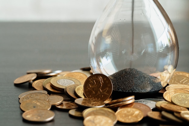 Time is money concept. Close up of hourglass with money coins