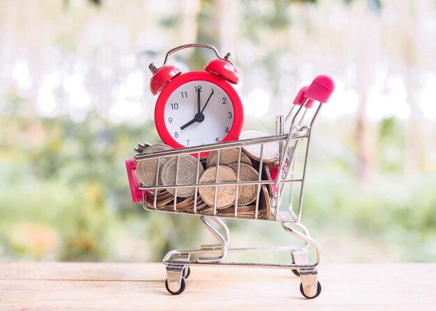 Time is money concept Red alarm and coins in shopping cart Save money for prepare in the future