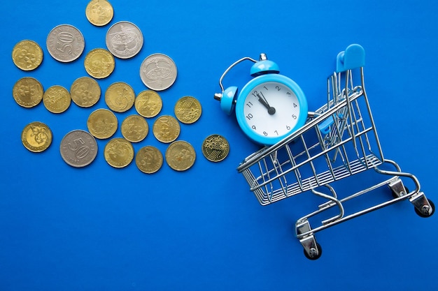 Time is money Shopping time Supermarket trolley with clock and coins on blue background Top view