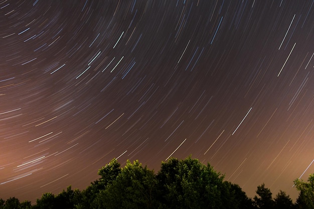 Photo a time lapse of a star trails above a forest