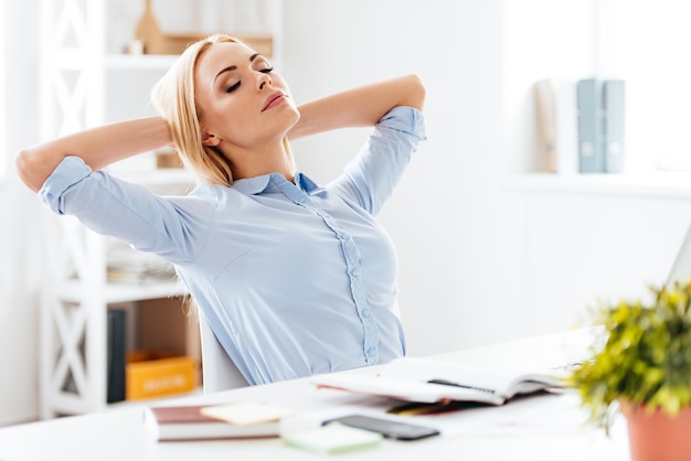 time for little rest. young beautiful woman holding hands behind her head and keeping eyes closed while sitting at her working place