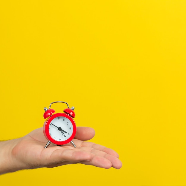 Concetto di gestione del tempo. mano con piccola sveglia rossa su sfondo di colore giallo alla moda