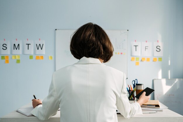 Photo time management planning weekly schedule for business owners managers young businesswoman manager standing in office in front of weekly schedule and sticking notes on wall