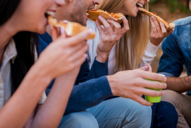 Time for pizza! Group of young people eating pizza while sitting outdoors