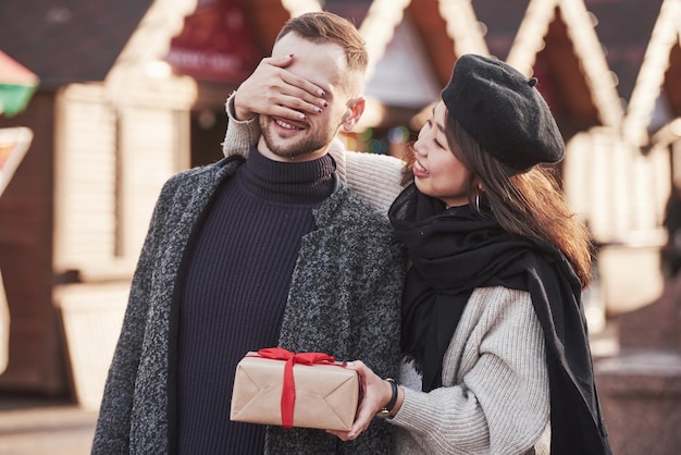 Time for presents. Holding gift box. Asian girl with her caucasian boyfriend.