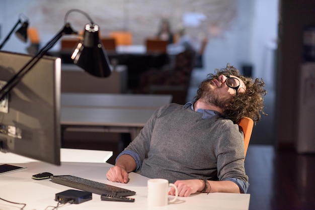 A time for relax. Young tired casual businessman relaxing at the desk in his night office