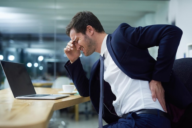 Time for some lumbar support Shot of a businessman wincing in pain and holding his lower back while sitting at a desk in an office