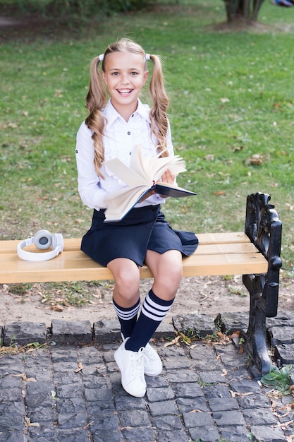 Time to study. Schoolgirl reading book. Little genius. Schoolgirl relaxing sit bench with book. Studying in school yard. Smart schoolgirl. Student adorable child in formal uniform relaxing outdoors.