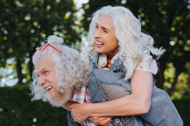 Time together. Nice happy man carrying his wife while spending pleasurable time together with her