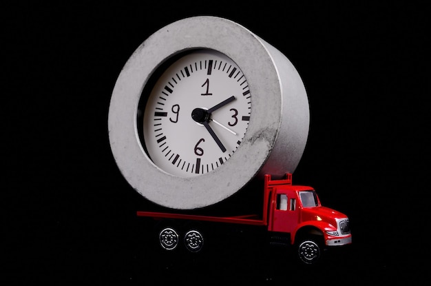 Foto tempo di trasporto concetto orologio orologio su un camion giocattolo rosso su sfondo nero