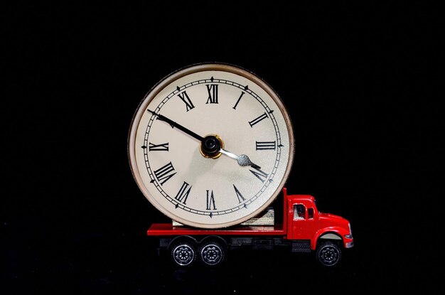 Foto tempo di trasporto concetto orologio orologio su un camion giocattolo rosso su sfondo nero