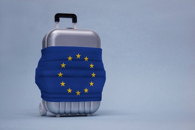 Time to travel. The concept of safe rest during a pandemic Covid-19 Coronavirus. Suitcase for travel with a medical mask and flag of the European Union.