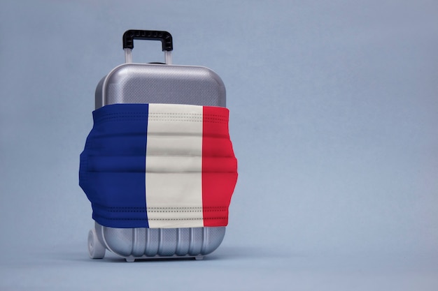 Time to travel. The concept of safe rest during a pandemic Covid-19 Coronavirus. Suitcase for travel with a medical mask and flag of France.