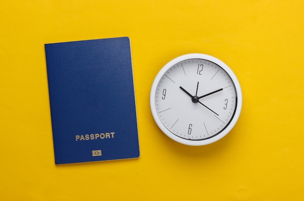 Time to travel. Passport and clock on yellow surface. Top view