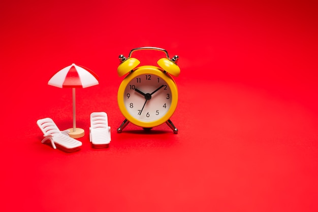 Time to travel. Sun lounger, umbrella and alarm clock on a red background.