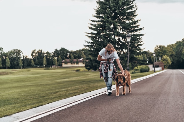 散歩の時間。屋外で時間を過ごしながら彼の犬と一緒に歩いているハンサムな若い男の全長