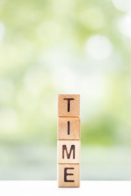 Time word is written on wooden cubes on a green summer background Closeup of wooden elements