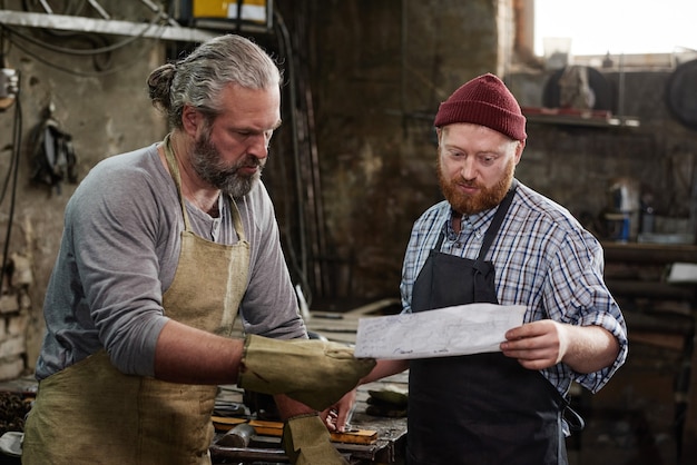 Foto timmerman bespreekt blauwdruk samen met de meester voordat hij aan het werk in de werkplaats begint