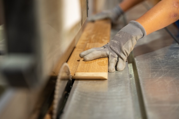 Timmerman die hout snijdt met een machine die oordopjes draagt.