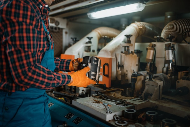 Timmerman in uniform in de buurt van houtbewerkingsmachine, houtindustrie, timmerwerk. Houtverwerking op fabriek, boszagen in houtzagerij