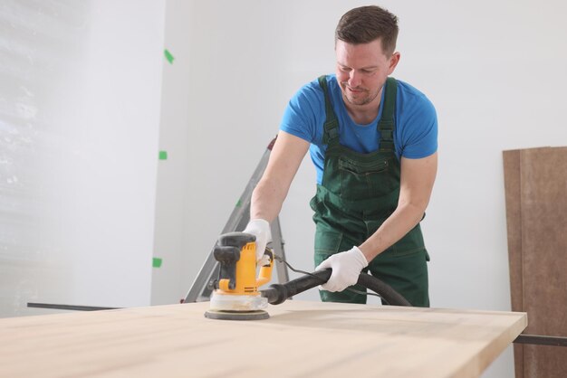 Timmerman in uniform polijst houten tafel met moderne slijpmachine man verwerkt hout