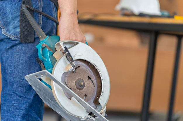 Timmerman man aan het werk in hout workshop Klusjesman handarbeider in gereedschapsriem en cirkelzaag in zijn handen houden