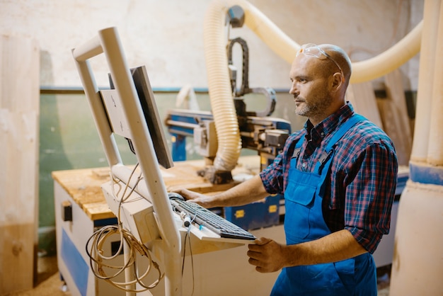 Timmerman op pc werkt met houtbewerkingsmachine, houtindustrie, modern timmerwerk. Houtverwerking op meubelfabriek, productie van producten van natuurlijke materialen