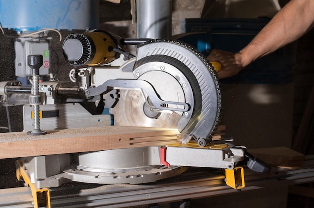 Timmerman werkt met elektrische cirkelvormige verstek om houten plank te snijden