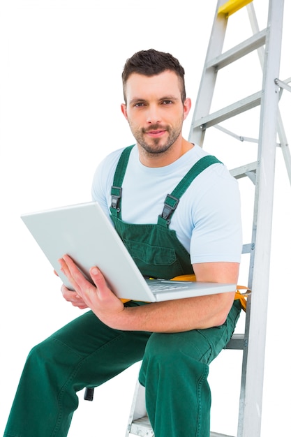 Timmerman zittend op de ladder met behulp van laptop