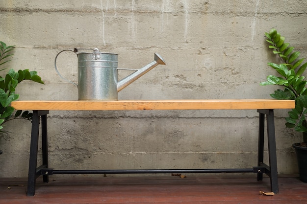 tin watering can on wooden bench with concrete wall in backyard