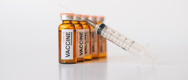 흰색 배경에 바늘이 달린 의료용 주사기와 라벨이 있는 착색 유리 백신 병. 복사 공간이 있는 의약품 광고 배너.