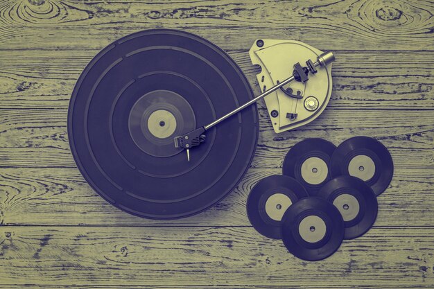 Tinted image of the player and vinyl discs on a wooden background. Retro technique for playing music.